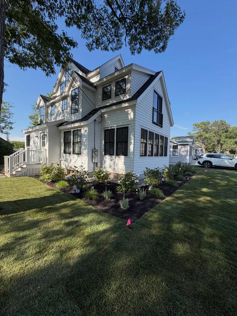 A lawn and newly planted beds around a white shingle home.