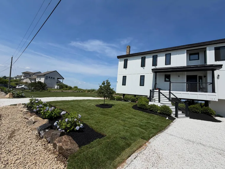 Finished lawn and planted beds beside a white house and gravel drive.