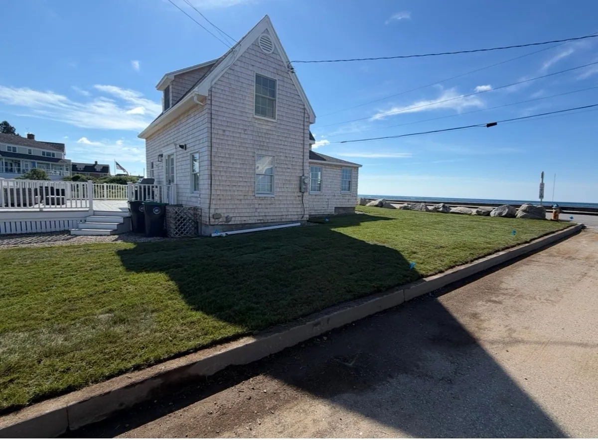 A green lawn around a shingle house beside the coast after renovation.