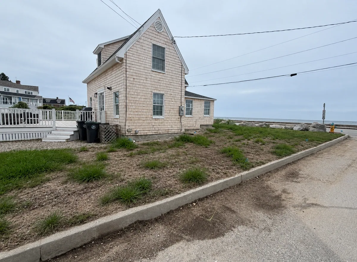Patchy grass and bare ground around a shingle house before renovation.