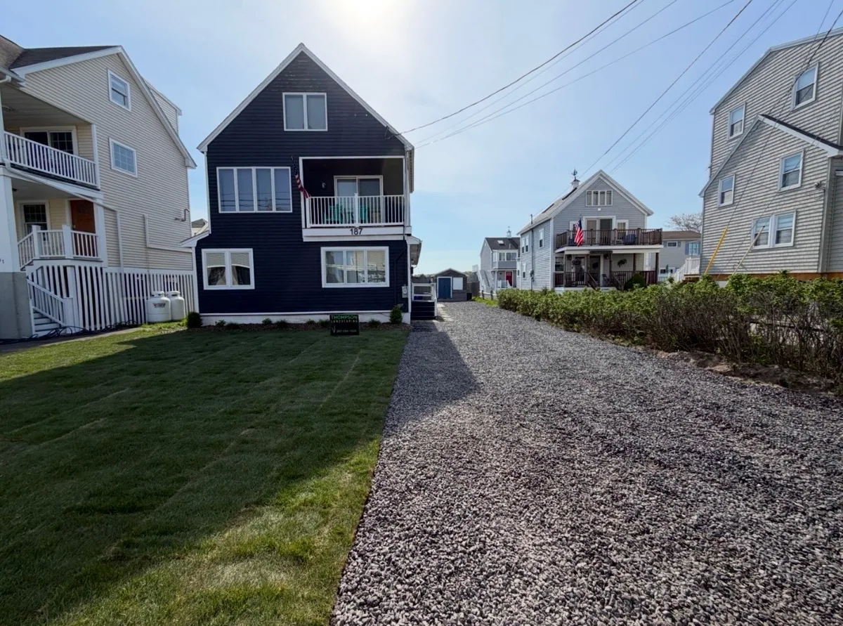A green lawn and gravel driveway beside the dark blue house after renovation.