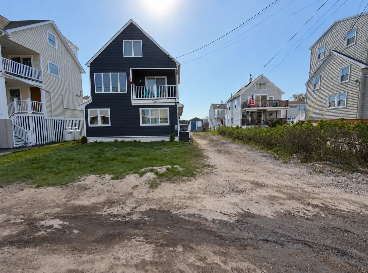 Uneven grass and a worn driveway area beside a dark blue house before renovation.